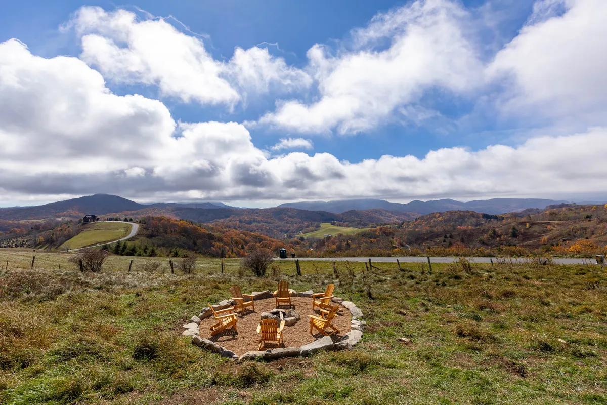 The image highlights a fire pit surrounded by Adirondack chairs, with scenic views stretching into the surrounding landscape. The area is designed for relaxed gatherings, stargazing, and sharing stories or s’mores under the open sky. The relaxed mood underscores the communal and tranquil outdoor experience described in the section.