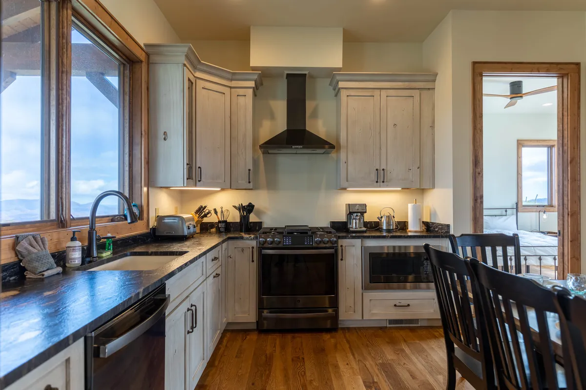 This image showcases the open-concept kitchen and dining area, featuring warm wooden cabinets, sleek black countertops, modern kitchen appliances, and a spacious dining table set for gatherings. The layout supports both culinary activity and communal dining, with ample space for family and friends to come together.