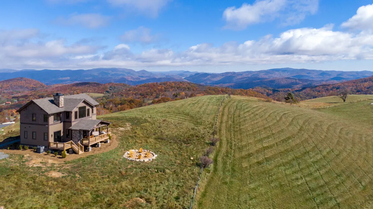 This wide exterior shot captures the house, the fire pit area, rolling hills, and distant mountains. The composition highlights the property’s spacious, secure outdoor environment, perfect for both children and pets. The scene radiates peace and opportunity for memory-making in the fresh mountain air.