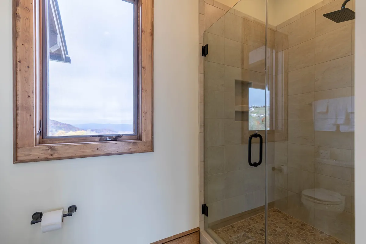 A stylish bathroom with natural stone flooring, a modern shower area with glass partitions, and a window offering scenic outdoor views. The space feels tranquil and refreshing, with high-end finishes and an abundance of natural light.