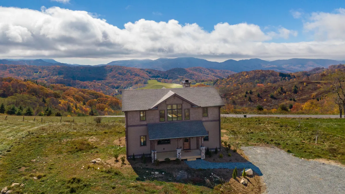A scenic exterior shot of Eagles Peak with the house nestled against a backdrop of rolling mountains covered in vibrant autumn foliage. The inviting porch looks out over the breathtaking landscape, hinting at opportunities for nature walks, hiking adventures, or simply relaxing while taking in the view.
